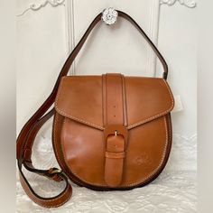 Padova Saddle Bag Classic Equestrian Style Is Easily Within Reach. This Crossbody Saddle Bag Perfectly Nods To Chic Sophistication No Matter The Occasion. You're Sure To Reach For It Time And Time Again Size/Profile: Petite Saddle Bag Walls: Full-Grain Leather Trim/Embellishments: Heavy, Hand-Crafted Stitching Handles/Strap: Adjustable, Flat Leather Crossbody Strap Exterior: Rear Slip Pocket Hardware: Metal Studs Closure: Flap Top With Magnetic Snap Closure And Buckle Lining/Trim: Faux Suede/Vel Cognac Saddle Bags With Adjustable Strap, Cognac Saddle Shoulder Bag For Daily Use, Everyday Saddle Bags With Leather Handles, Daily Use Saddle Flap Bag With Leather Lining, Cognac Saddle Bag With Removable Pouch, Leather Lined Saddle Flap Bag, Everyday Saddle Flap Bag With Leather Lining, Saddle Flap Bag With Leather Lining For Everyday, Saddle Bag With Adjustable Strap For Daily Use