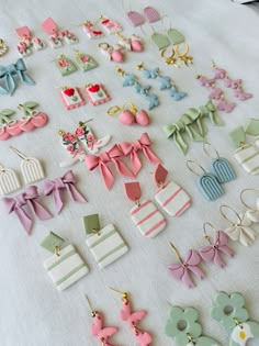 many different types of earrings are laid out on a white tablecloth with pink, green and blue bows