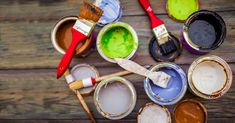 several paint cans with different colors of paint and brushes in them on a wooden surface