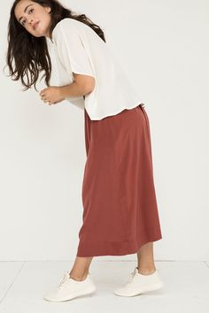 a woman is posing for the camera in a white shirt and brown skirt with her hands on her hips