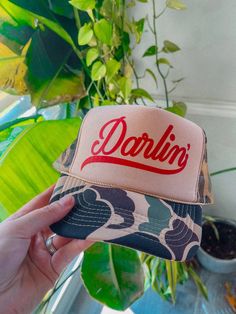 Show of your style in our Darlin' Country Western trucker hat. - Features the phrase "Darlin' " across the front in a red ink on a tan/camo hat- Come with a removable small brown pin attached to each hat - Individually heat pressed onto each hat - 5 Panel, Mesh Back with Snap Back *due to screens & filters colors may vary slightly to photos* Western Trucker Hats, Trucker Hat Ideas, Camo Hat, Maxi Dress Pattern, Western Chic, Hat Ideas, Sporty And Rich, Snap Back, Red Ink