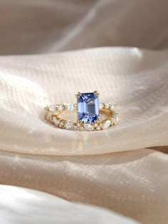 an engagement ring with a large blue stone surrounded by small white and yellow diamonds on a light colored fabric