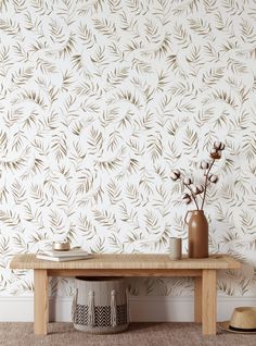 a wooden bench sitting in front of a wallpapered wall with leaves on it