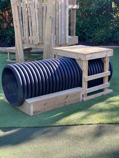 a wooden chair sitting on top of a lush green field next to a giant black hose