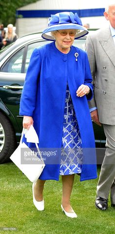 an older woman wearing a blue coat and matching hat walks next to a man in a suit