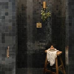 a black tiled shower with a wooden stool and potted plant on the wall next to it