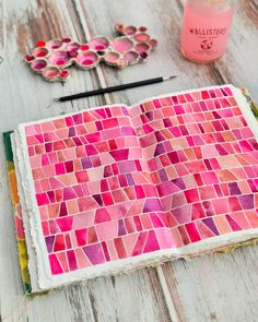 an open book with pink and red tiles on it next to some paintbrushes