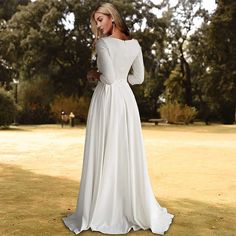 a woman in a white wedding dress standing on the grass with her back to the camera