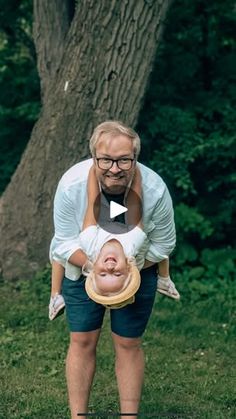 a man holding a baby up to his face in front of a tree and grass area