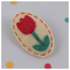 a red and green felt flower on a white background