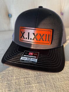 a black and grey hat with an orange patch on the front that says xj xxii