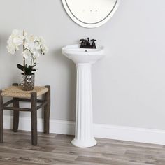 a white pedestal sink sitting next to a round mirror on the side of a wall