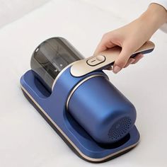 a person using a blue coffee maker on top of a white table with a cell phone in it