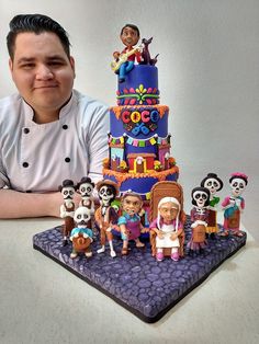 a man sitting in front of a large cake with cartoon characters on it and a chef next to it