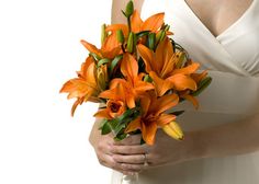 a woman in a white dress holding a bouquet of orange lilies and green leaves