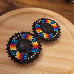 These earrings are made with seed beads and black centers encircled in black rhinestone. They are then branded with our logo, backed with moose hide and your choice of earring findings. The edging is done with black rondelle beads, creating and extra bit of sparkle as the earrings move about. Each pair are made with hypoallergenic materials for sensitive ears. You can now upgrade your earring to include a tassel attachment. This upgrade allows you to have a 3 in 1 pair of earrings. The tassel ea Beaded Earrings With Cabochon Centers, Round Beaded Earrings, Indigenous Beading, Indigenous Style, Beaded Studs, Native Beading, Seed Bead Jewelry Patterns, Native Beading Patterns, Beaded Earrings Native