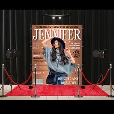 a woman standing in front of a poster on a red carpeted area with black curtains