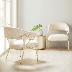 two chairs and a table in a white room with a plant on the end table