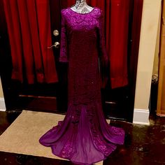 a purple dress on display in front of a red curtained area with a mannequin's head