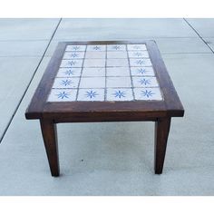 a wooden table with white and blue tiles on it's top sitting on the sidewalk