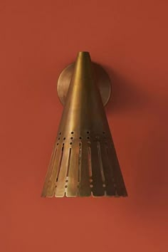 a wall mounted light on the side of a red wall with a metal cone hanging from it