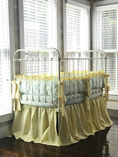 a baby crib with yellow ruffled bedding in front of two large windows