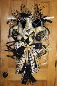 a mask hanging on a door with black and gold ribbons around it's face