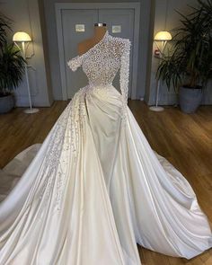 a white wedding dress with long sleeves and beading on the shoulders, in front of a