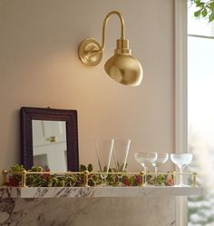 a shelf with wine glasses on it next to a mirror and a wall mounted light