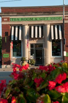 a store front with red flowers in the foreground and an american flag on the window