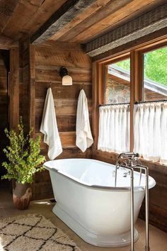 a white bath tub sitting in a bathroom next to a window with curtains on it