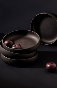 three bowls and two plates with fruit in them on a black surface, next to one another