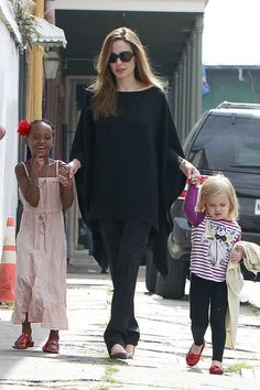 the woman is walking with two small girls on her hand and another child holding hands