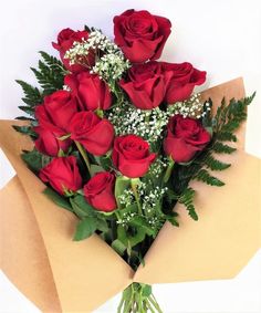 a bouquet of red roses wrapped in brown paper with greenery and baby's breath