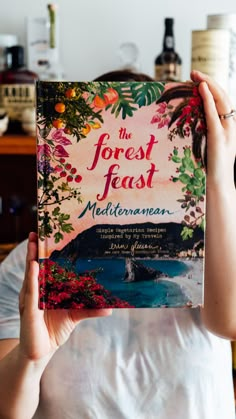 a woman holding up a book in front of her face with the title, the forest feast