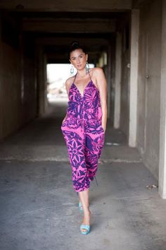 a woman is walking down an alley way in a pink and purple jumpsuit with blue heels