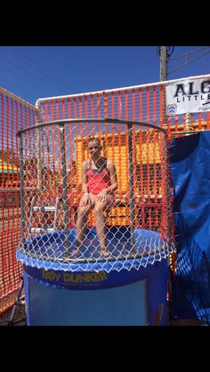 a woman sitting on top of a blue trampoline in front of an orange fence