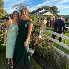 two women standing next to each other in front of a white fence and flower garden