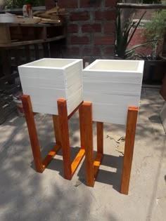 two white wooden tables sitting next to each other on a cement floor in front of a brick wall