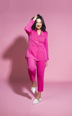 a woman in a pink suit and white shoes posing with her hands on her head