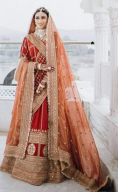 a woman in a red and gold bridal gown standing by a window with her hands on her hips