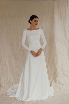 This unique wedding dress, made from luxurious crepe, is an ideal minimalistic elegance. With long sleeves and an A-line silhouette, this floor-length gown with a long train is perfect for winter weddings, including Christmas or civil ceremonies.  The modest design features a flattering boat neckline and a high back, creating a timeless and graceful look. Bridal buttons flow down the back and extend to the end of the train, adding a touch of classic beauty, long sleeves are also complemented wit Timeless Wedding Dress Modest, A Line Long Sleeve Wedding Dress, Long Sleeve Wedding Dress Winter, Christmas Wedding Dress, Bridal Buttons, Wedding Dresses Modest, Wedding Dress Winter, Long Sleeves Wedding Dress, Modest Wedding Dresses With Sleeves