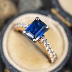 an engagement ring with a blue stone surrounded by white and clear stones in a box