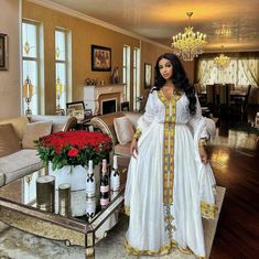 a woman standing in a living room next to a table with red flowers on it