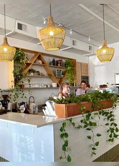 two people sitting at a counter in a restaurant with plants growing on the wall and hanging from the ceiling