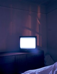 a television sitting on top of a wooden dresser in a room with light coming through the window