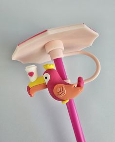 a pink toy umbrella with a bird on it's handle and a cup in its mouth