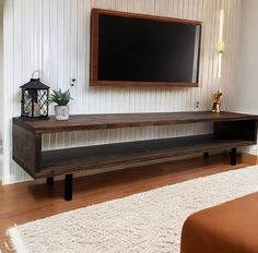 a flat screen tv sitting on top of a wooden shelf next to a white rug