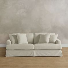 a white couch sitting on top of a hard wood floor next to a gray wall