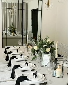 a long table set with black and white place settings, candles and flowers in vases